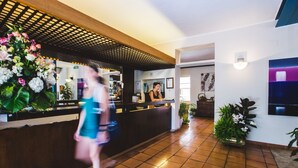 A hotel reception area with a tiled floor, a reception desk, and a large floral arrangement. - Hotel Sabrina (Castiglione della Pescaia)