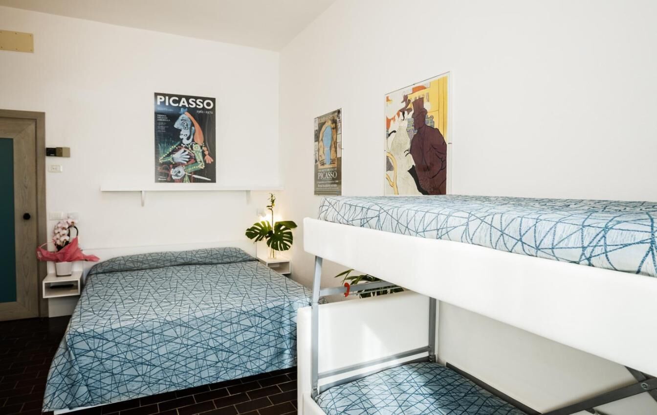 Un dormitorio con literas, carteles en la pared, una mesita de noche con una planta y una puerta.