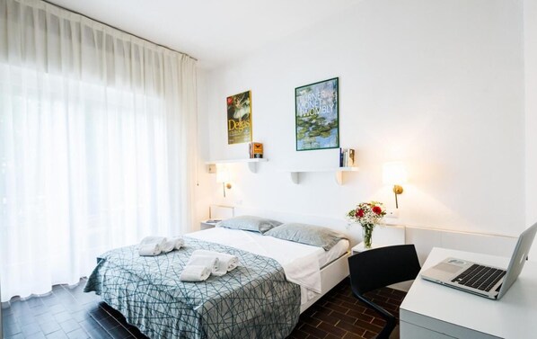 Une chambre d’hôtel comprenant un lit, un bureau avec un ordinateur portable, une chaise et deux lampes fixées au mur.