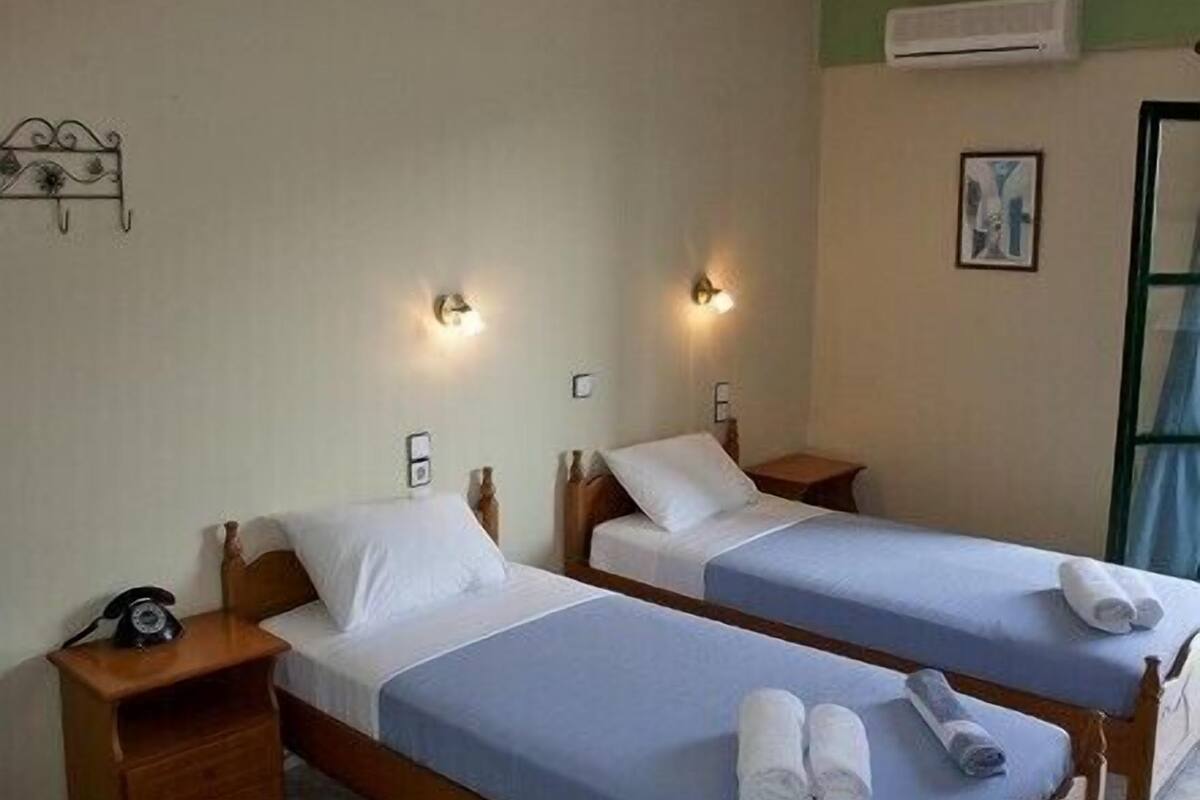 A hotel room with two single beds, bedside tables, a wall-mounted telephone, and a painting.
