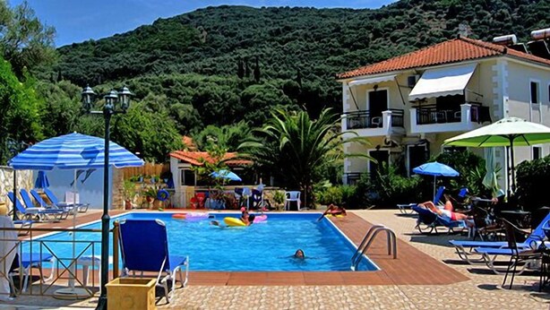 A pool area with lounge chairs and umbrellas, surrounded by greenery and a hillside. - Harmony Resort (Parga)