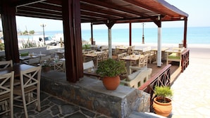 Un espacio de comedor al aire libre con suelo de piedra, mesas y sillas de madera, y plantas en macetas.