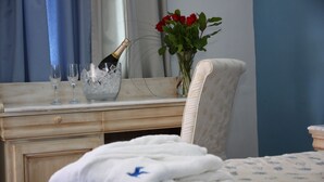 Habitación de hotel con cama, mesita de noche con una botella de champán, copas y un jarrón con rosas rojas.