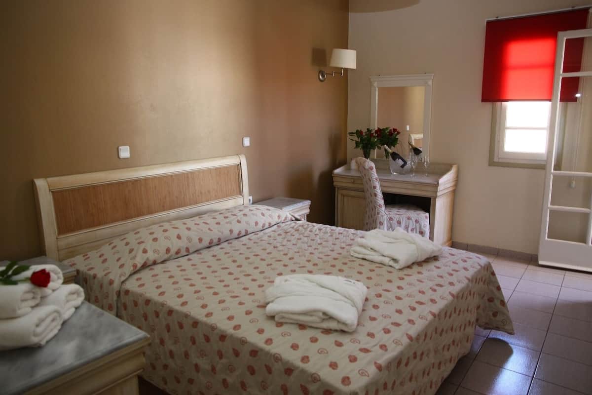 Quarto com cama, mesas de cabeceira, penteadeira, espelho e janela com cortina vermelha.