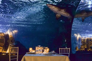 An underwater dining area with a table set for two, surrounded by large aquarium tanks with sharks.