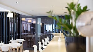 A modern restaurant with white tables and chairs, a long counter, and a potted plant. - Hotel Alpha (Fribourg)