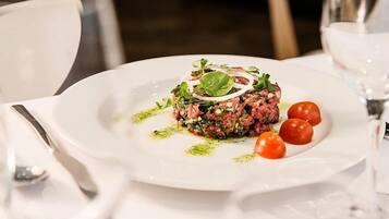 Ein weißer Teller mit einem Fleischgericht, dekoriert mit Salat und Kirschtomaten, auf einer weißen Tischdecke.