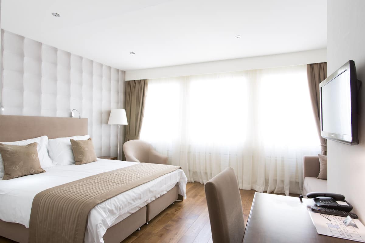 Quarto de hotel com uma cama grande, uma mesa com telefone e uma televisão na parede.