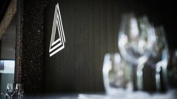 A restaurant interior with a modern geometric logo on the wall, a table with glasses, and a blurred background suggesting a dining area.