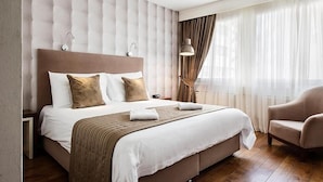 A hotel room with a large bed, a headboard, a nightstand, a lamp, and a chair. - Hotel Alpha (Fribourg)