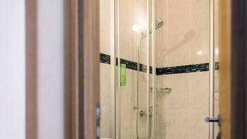 A glass-enclosed shower stall with a white tiled floor, a green towel rack, and a door with a blue handle.