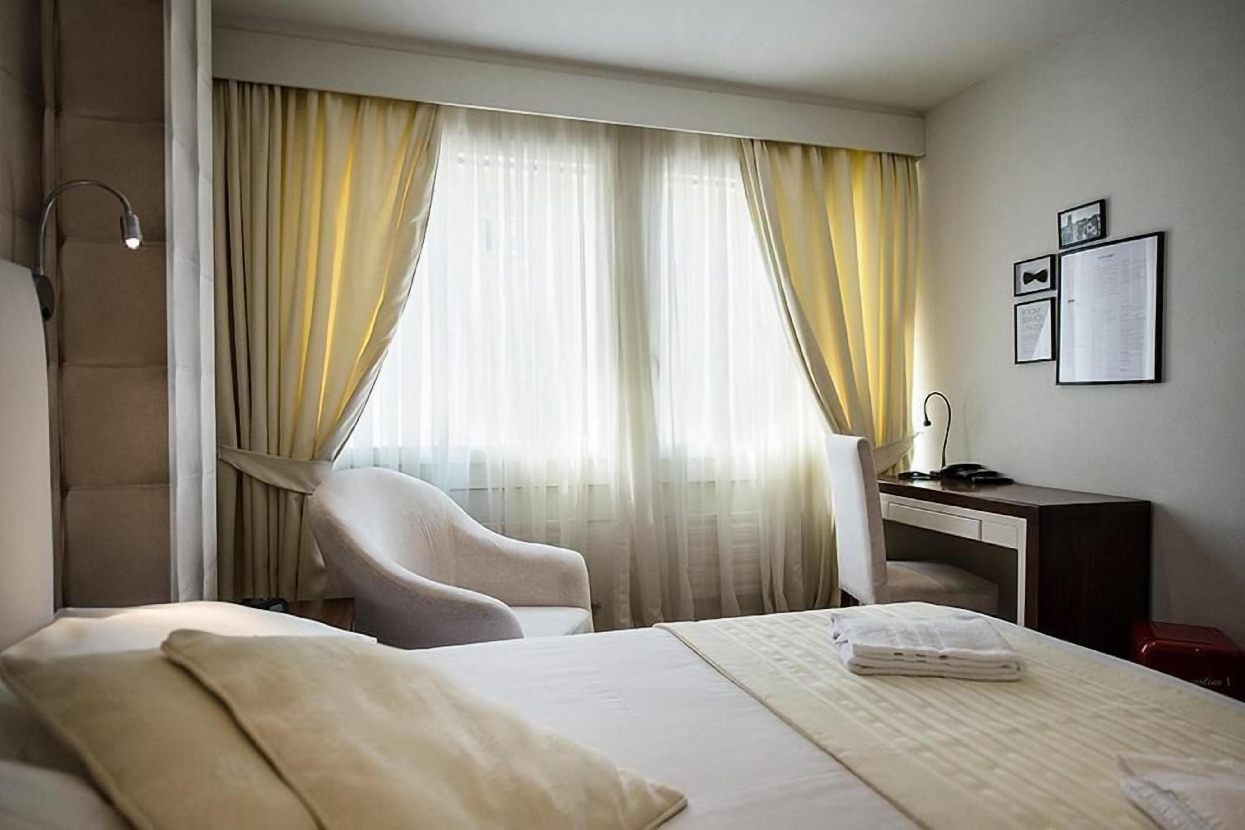 A hotel room with a bed, a desk, a chair, and curtains.