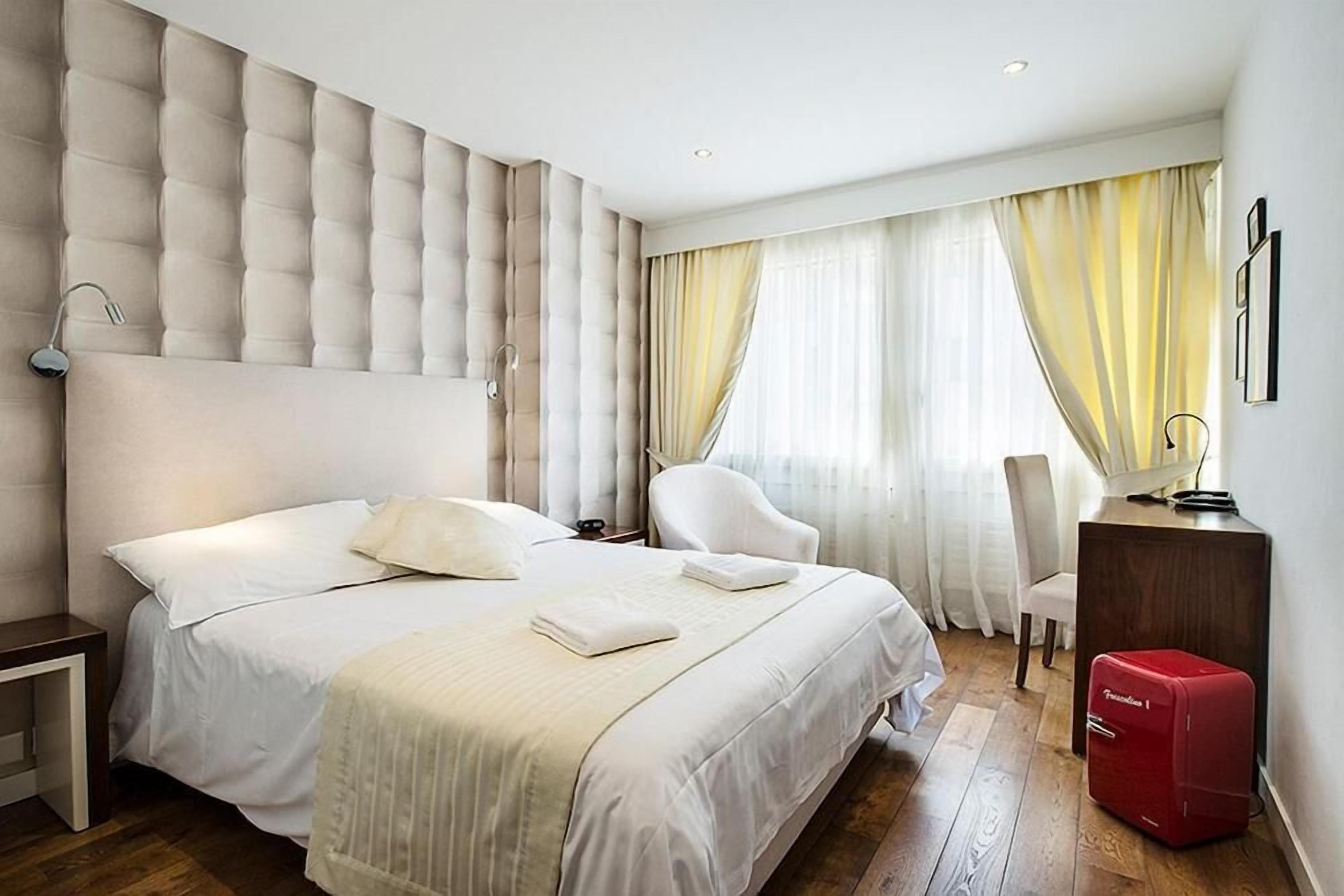 Une chambre d’hôtel avec un grand lit, une table de chevet, une chaise, un bureau et une valise rouge.
