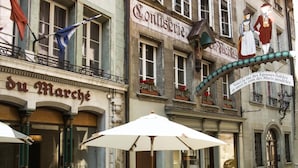 A street with outdoor seating, a man sitting at a table, and buildings with signs. - Hotel Alpha (Fribourg)