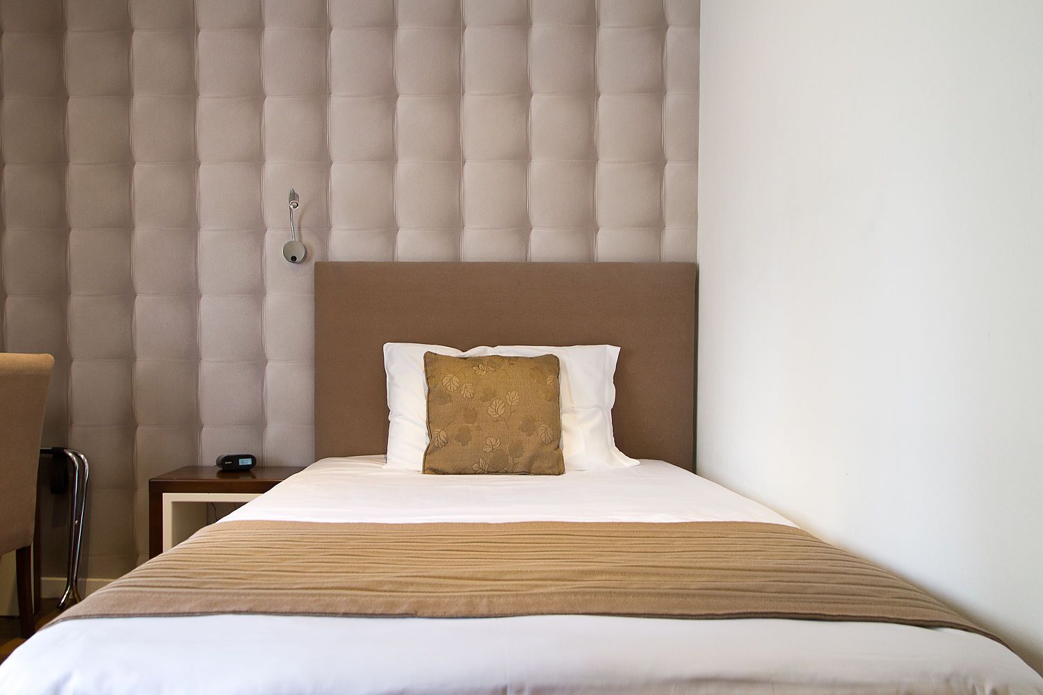 Een hotelkamer met een bed, nachtkastje en stoel.