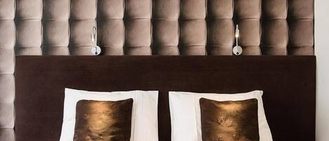 A double bed with two pillows, a dark headboard, and a wall with a tufted panel design.