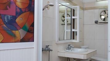 A bathroom with a white sink, a toilet, and a shower. There is a colorful abstract painting on the wall.