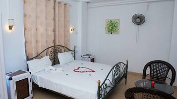 Una camera da letto ordinata con un letto, comodini, una sedia e una ventola.