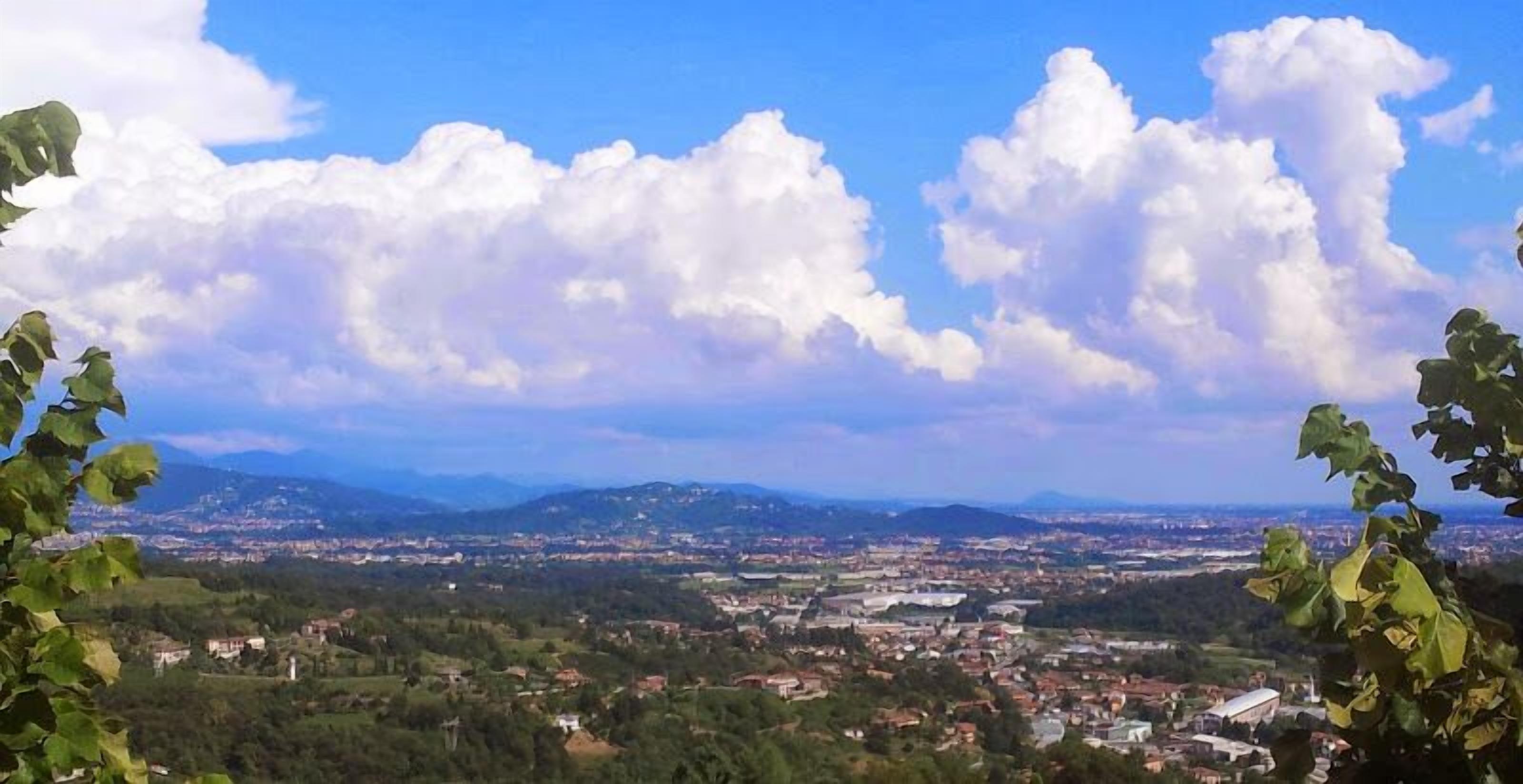 A panoramic view of a town with a mix of residential and commercial buildings, surrounded by hills and mountains.