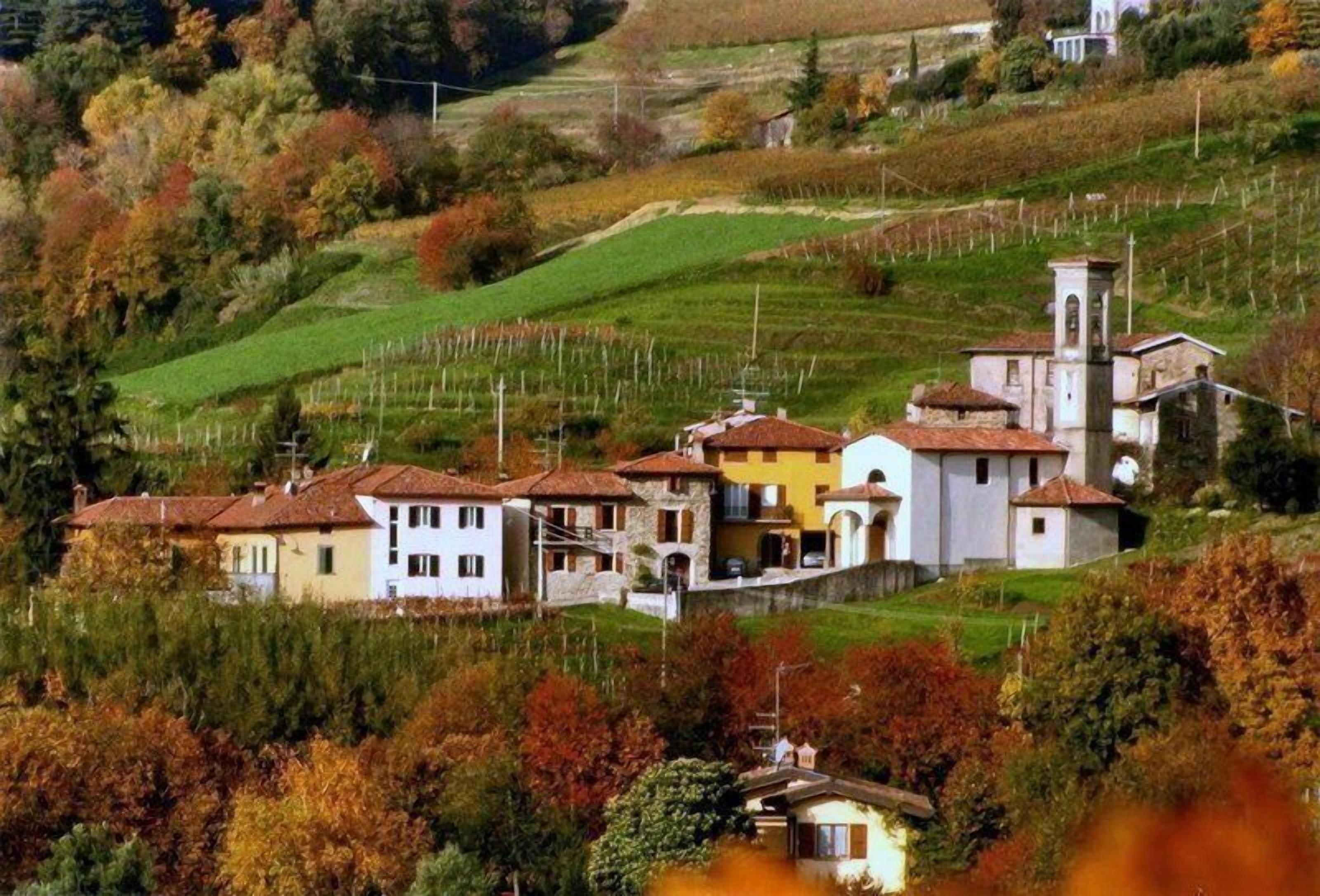 Un borgo collinare con edifici tradizionali, tra cui una chiesa con campanile, immerso tra vigneti.
