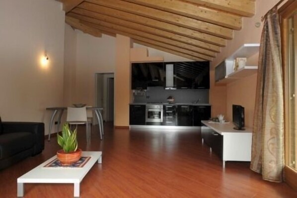 A spacious living area with a wooden ceiling, a dining table, and a kitchen in the background.