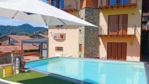 Una piscina con sillones blancos y una sombrilla blanca.