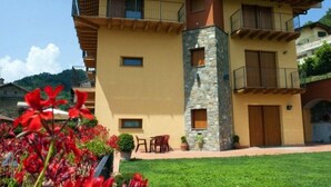 Un edificio de dos plantas con fachada de piedra, balcones y un pequeño jardín con flores rojas.