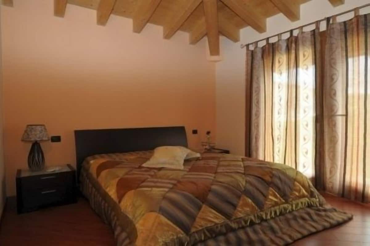 Une chambre à coucher avec un lit, une table de chevet, une lampe et une fenêtre avec des rideaux.