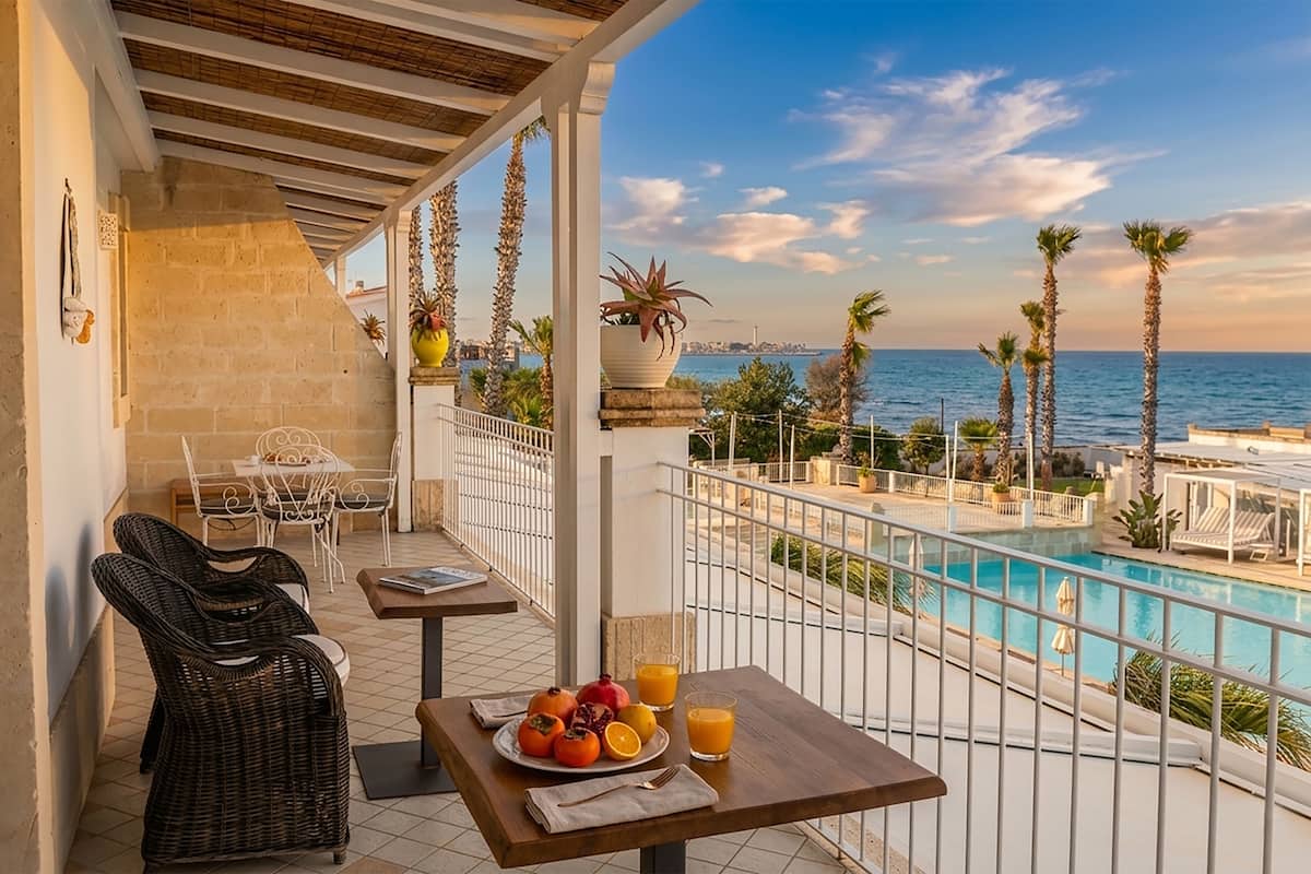 Un balcon avec des fauteuils en osier, une table avec des fruits et du jus, et une vue sur la mer.