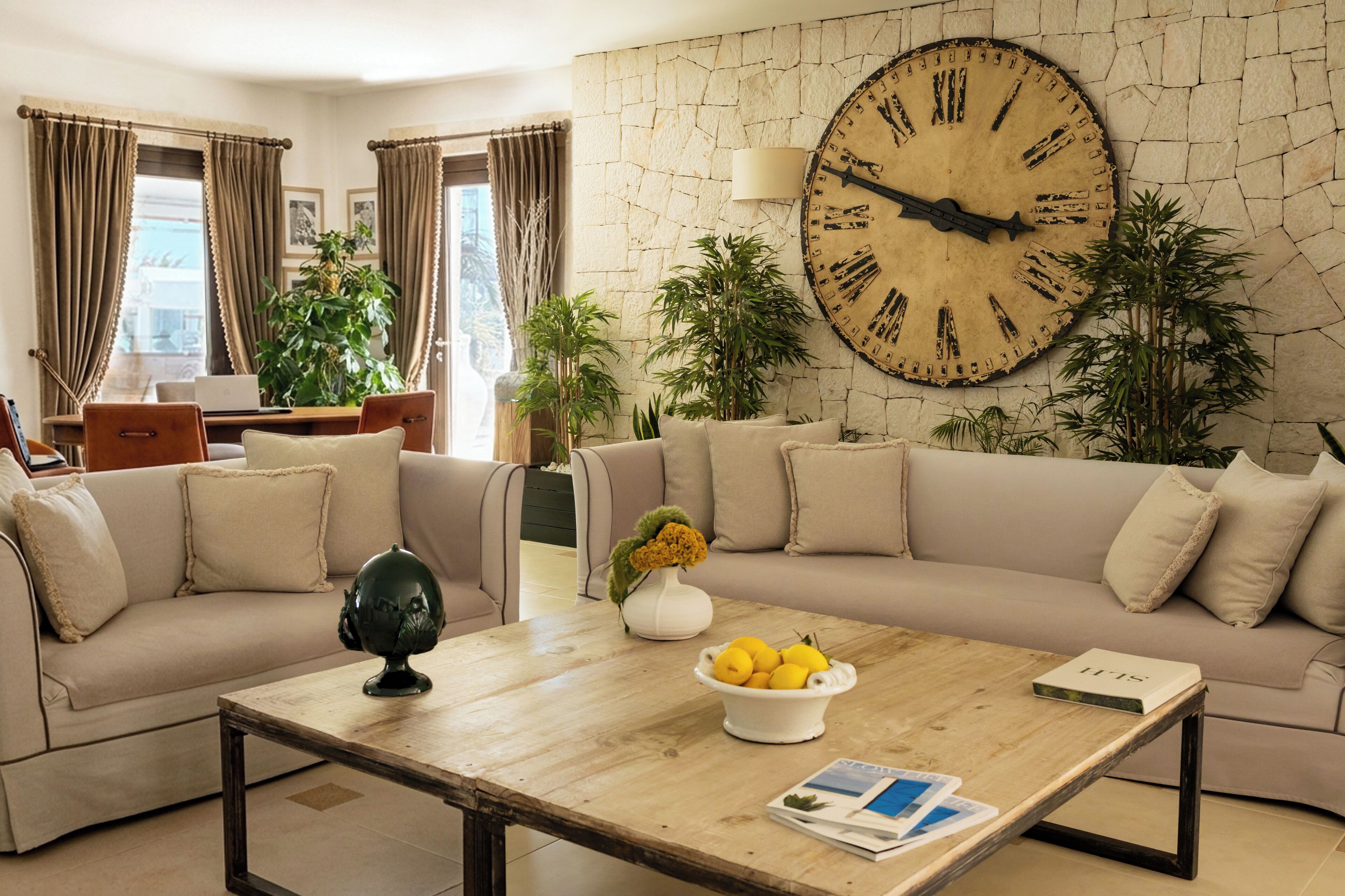 A living room with a large wall clock, a wooden coffee table with a bowl of lemons, a sofa, and a lamp.