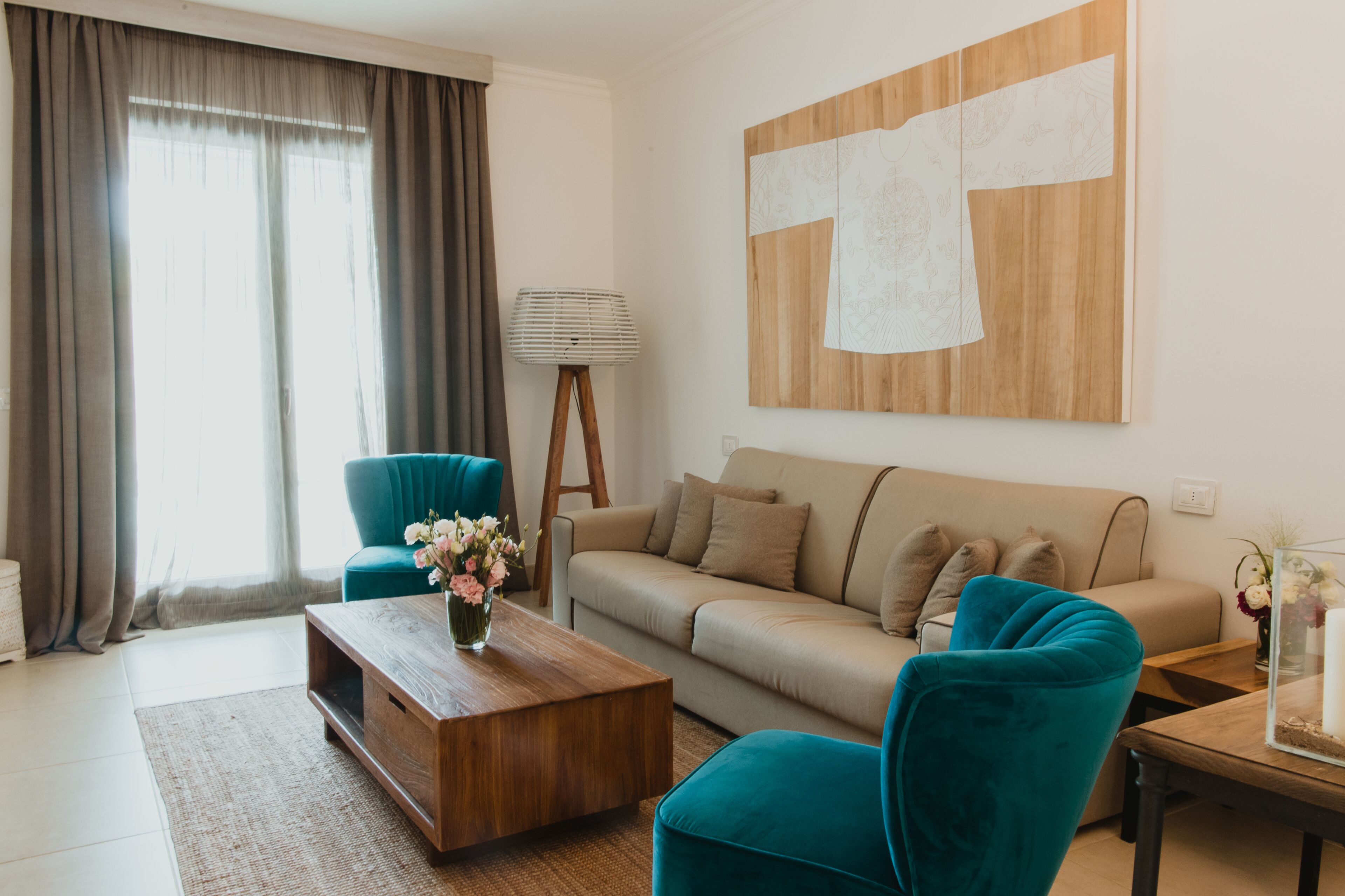 A modern living room with a sofa, two teal armchairs, a wooden coffee table, and a lamp.