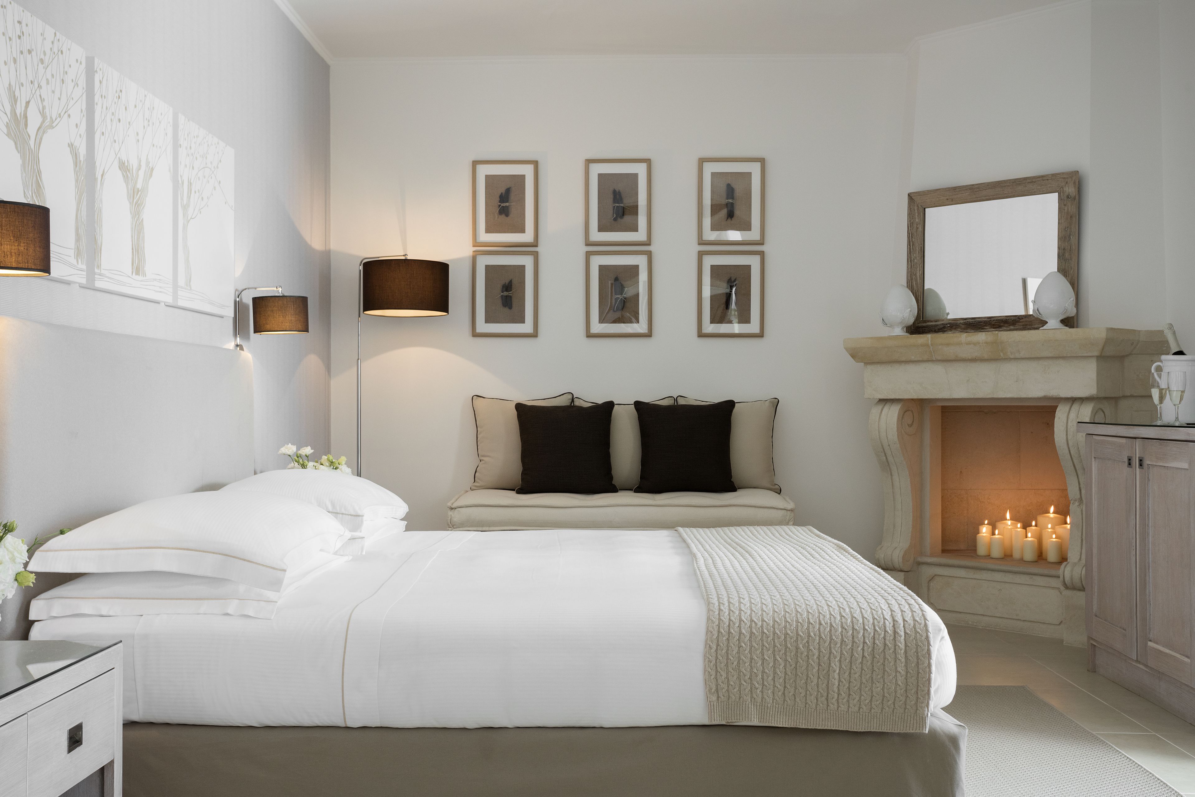 Una camera da letto con un letto grande, un comodino, una lampada a parete, quadri incorniciati, uno specchio e un camino con candele.