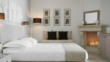 Una camera da letto con un letto grande, un comodino, una lampada a parete, quadri incorniciati, uno specchio e un camino con candele.