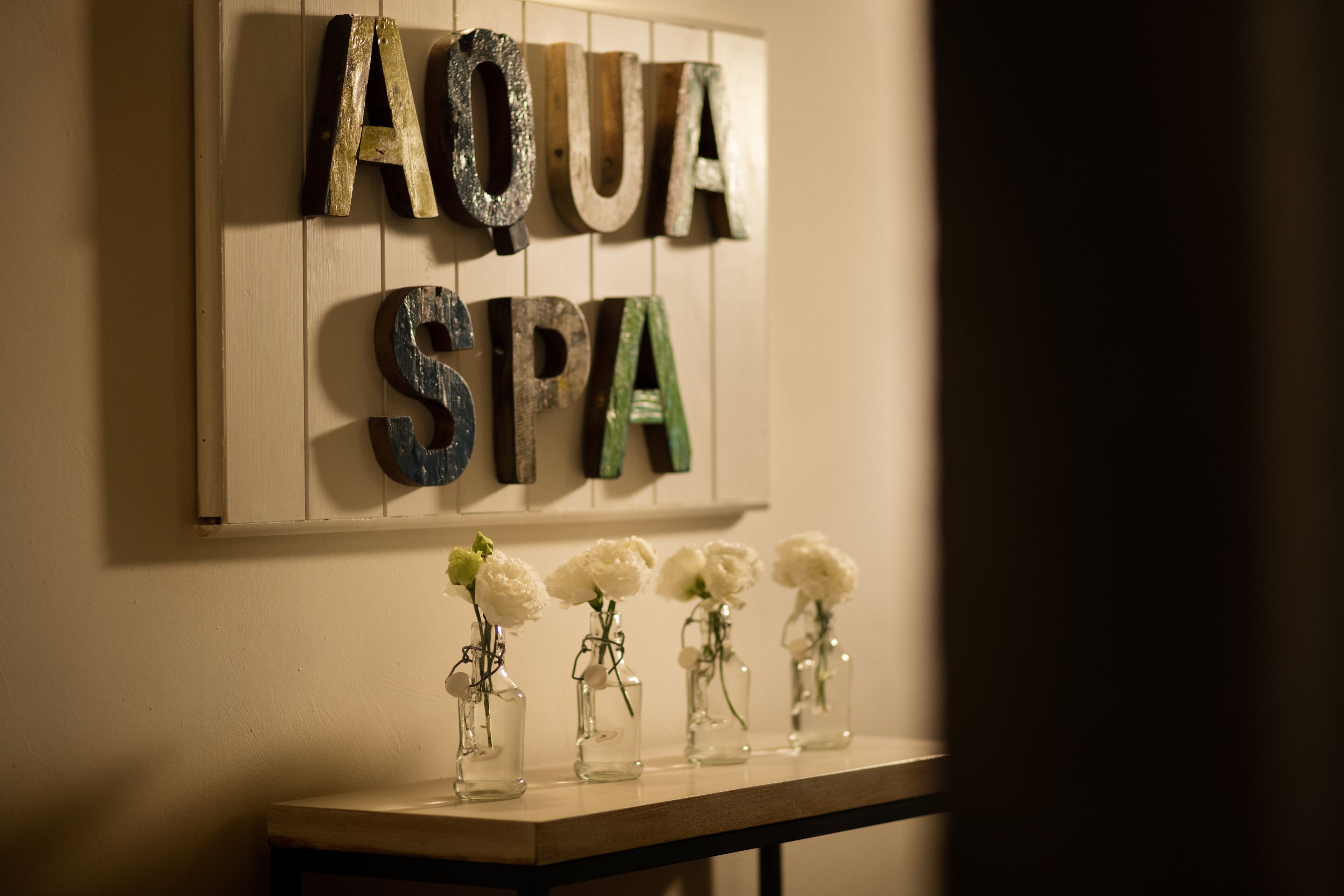 Pared con las palabras "AQUA SPA" y cuatro pequeños jarrones con flores blancas.