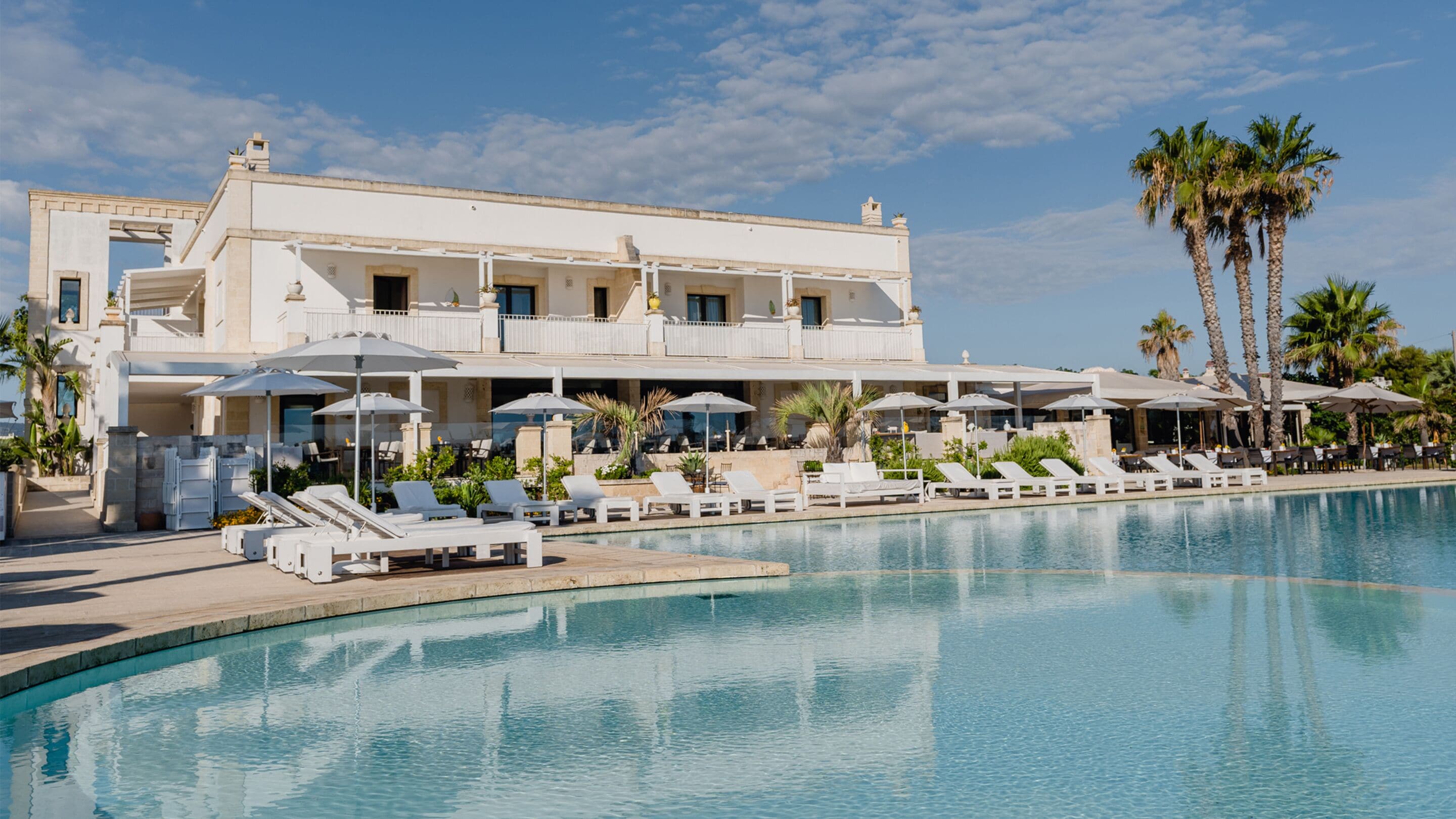 Un resort con piscina, camastros, sombrillas y palmeras.