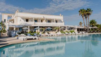 Un resort con piscina, camastros, sombrillas y palmeras.