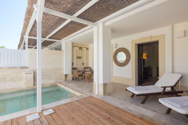 Un área de piscina techada con sillones de descanso, una mesita y una silla de mimbre.