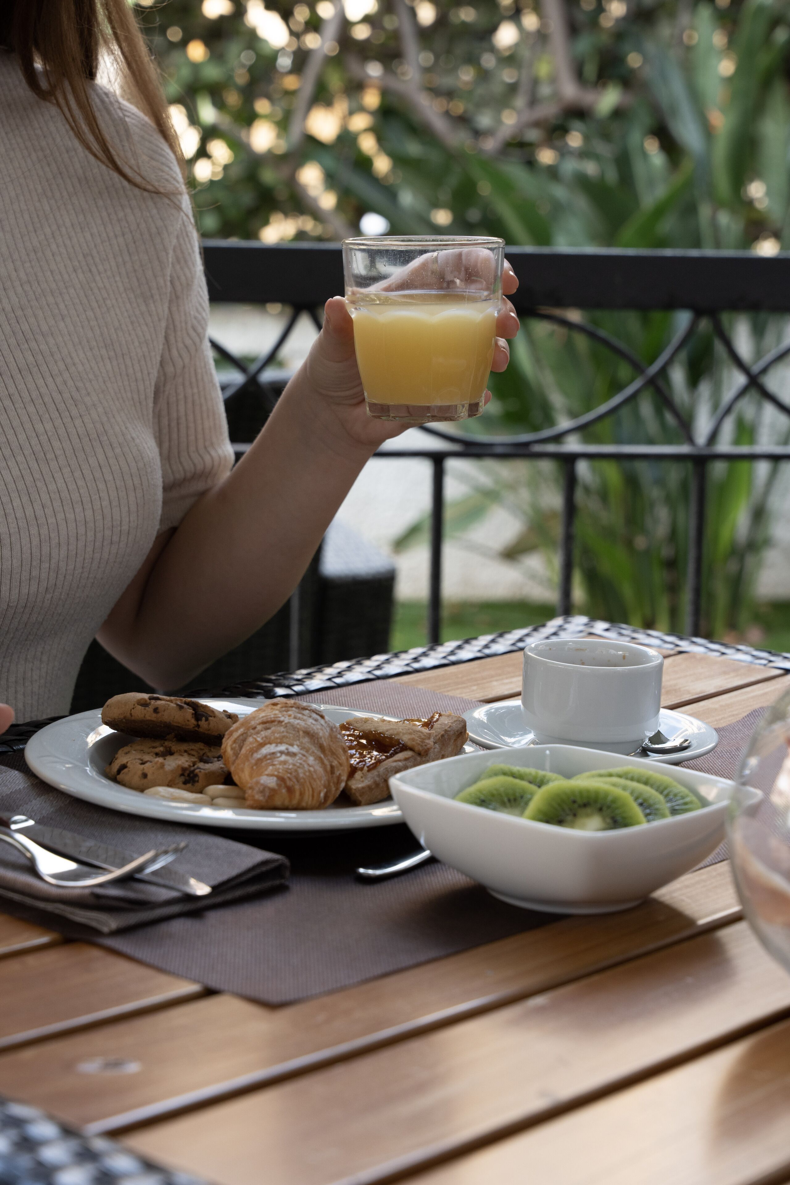 Una persona seduta a un tavolo all'aperto con un piatto di cibo, un bicchiere di succo d'arancia e una ciotola di kiwi a fette.