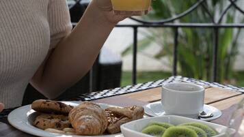 Una persona seduta a un tavolo all'aperto con un piatto di cibo, un bicchiere di succo d'arancia e una ciotola di kiwi a fette.