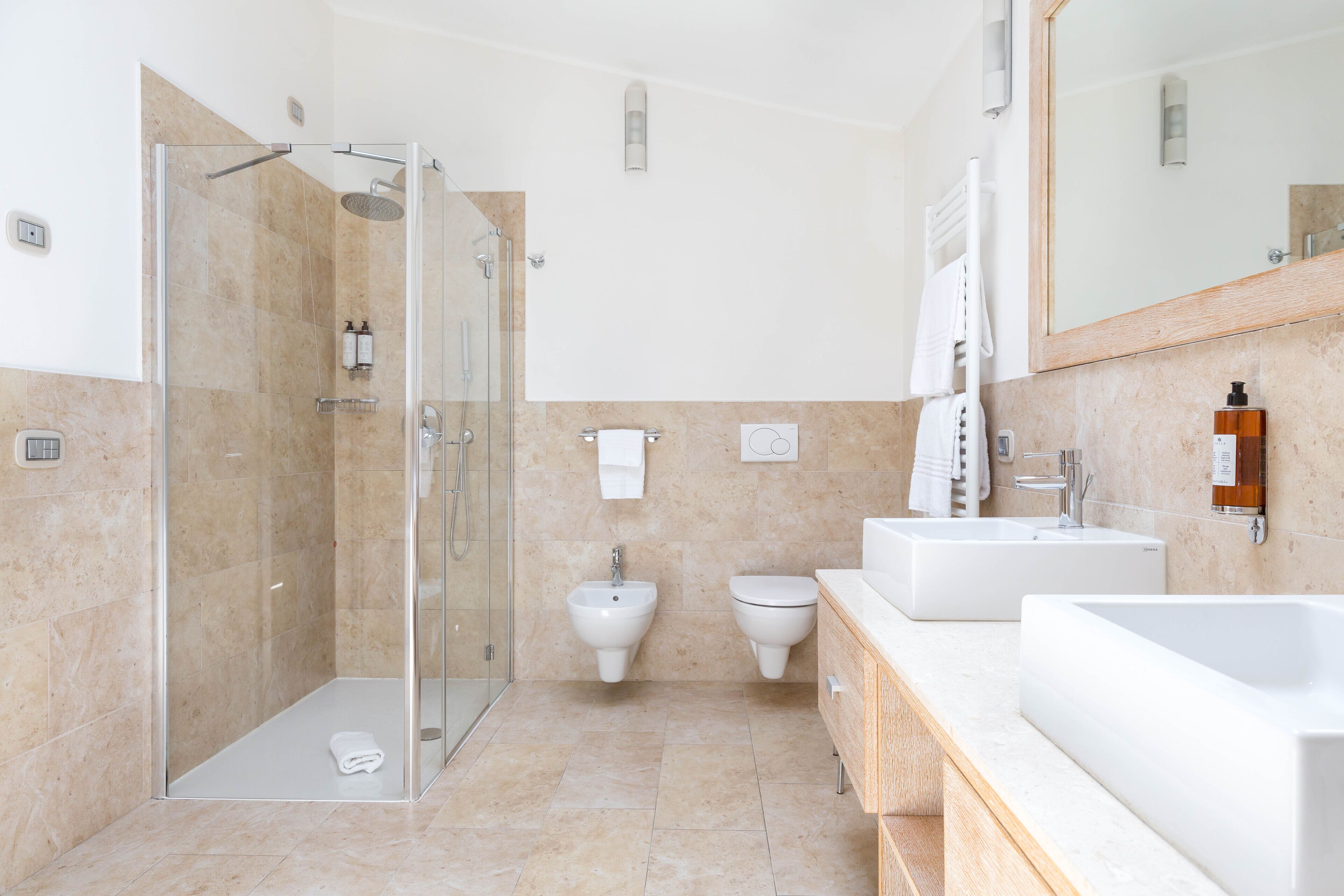 Une salle de bain moderne dotée d’une douche à parois de verre, d’un lavabo, d’un bidet et d’un grand miroir.