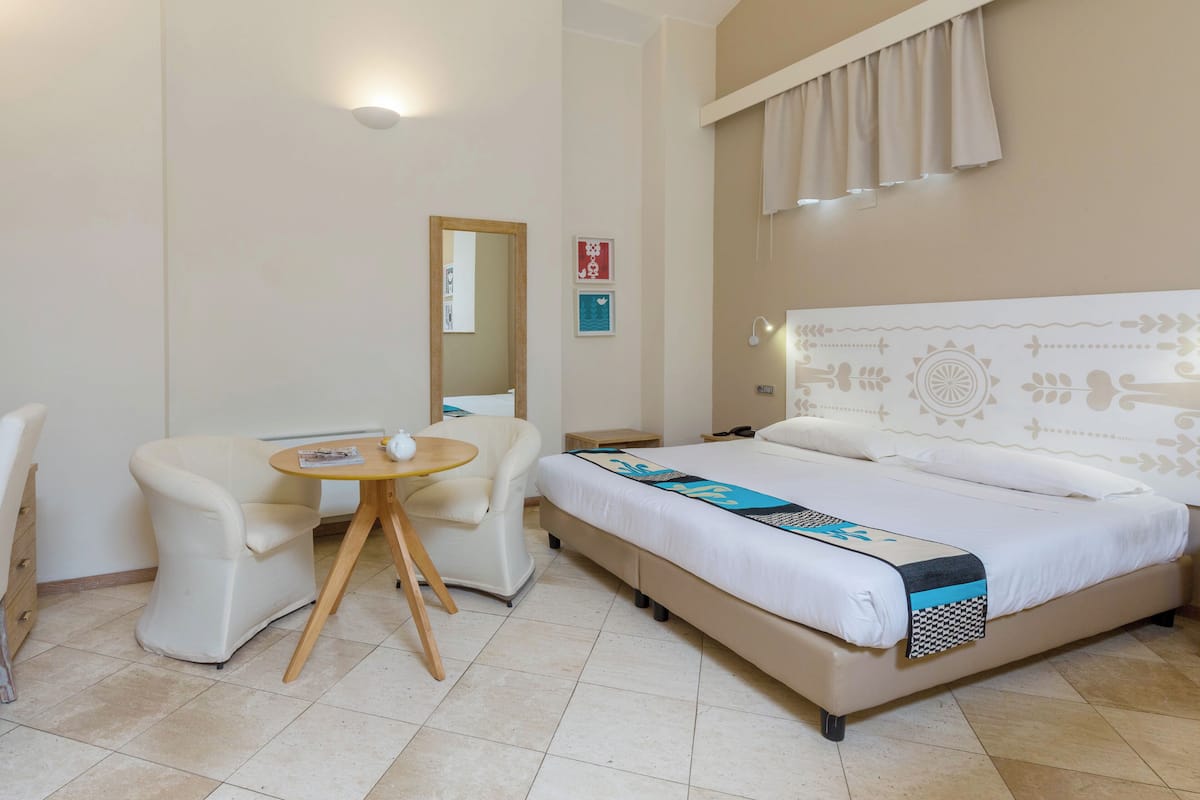 A hotel room with a bed, a chair, a small table, and a mirror.