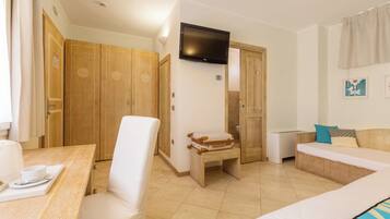 Une chambre d’hôtel comprenant un lit, une petite table avec un plateau, une chaise, un banc en bois, un téléviseur fixé au mur et une armoire en bois.