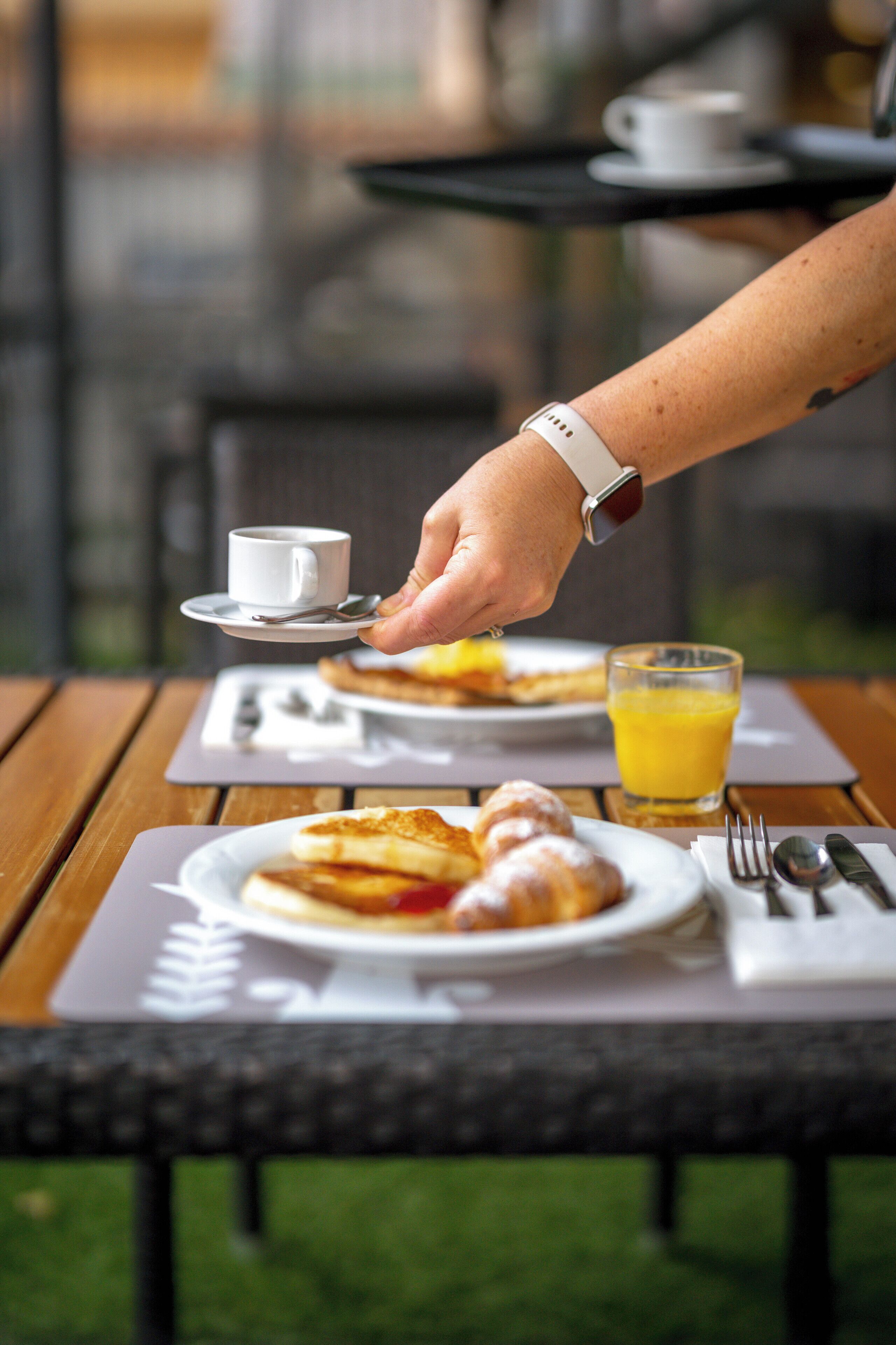 En frukostuppdukning med en tallrik bakverk, en kopp kaffe och ett glas apelsinjuice på ett träbord.