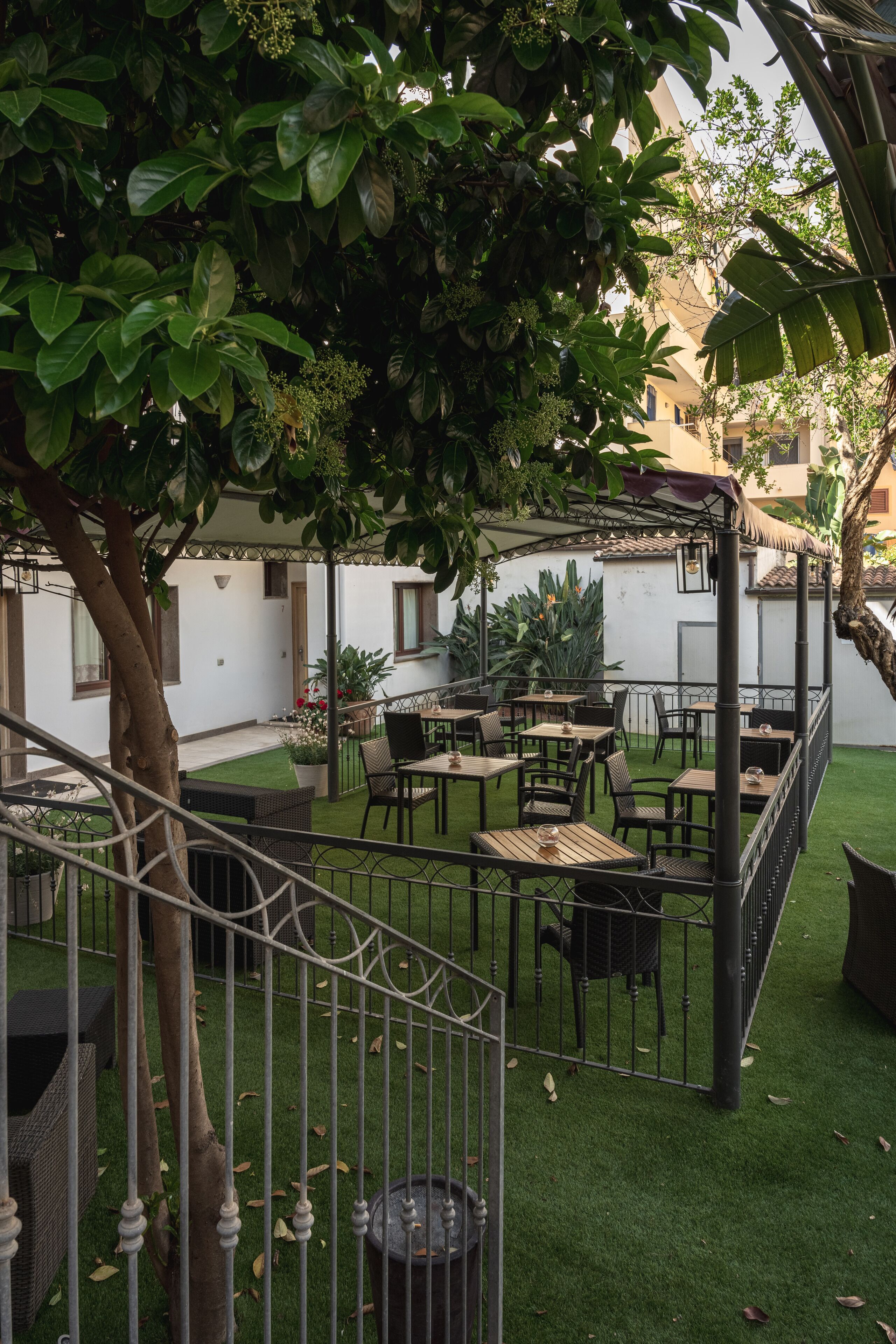An outdoor patio area with tables and chairs, surrounded by greenery and a staircase.