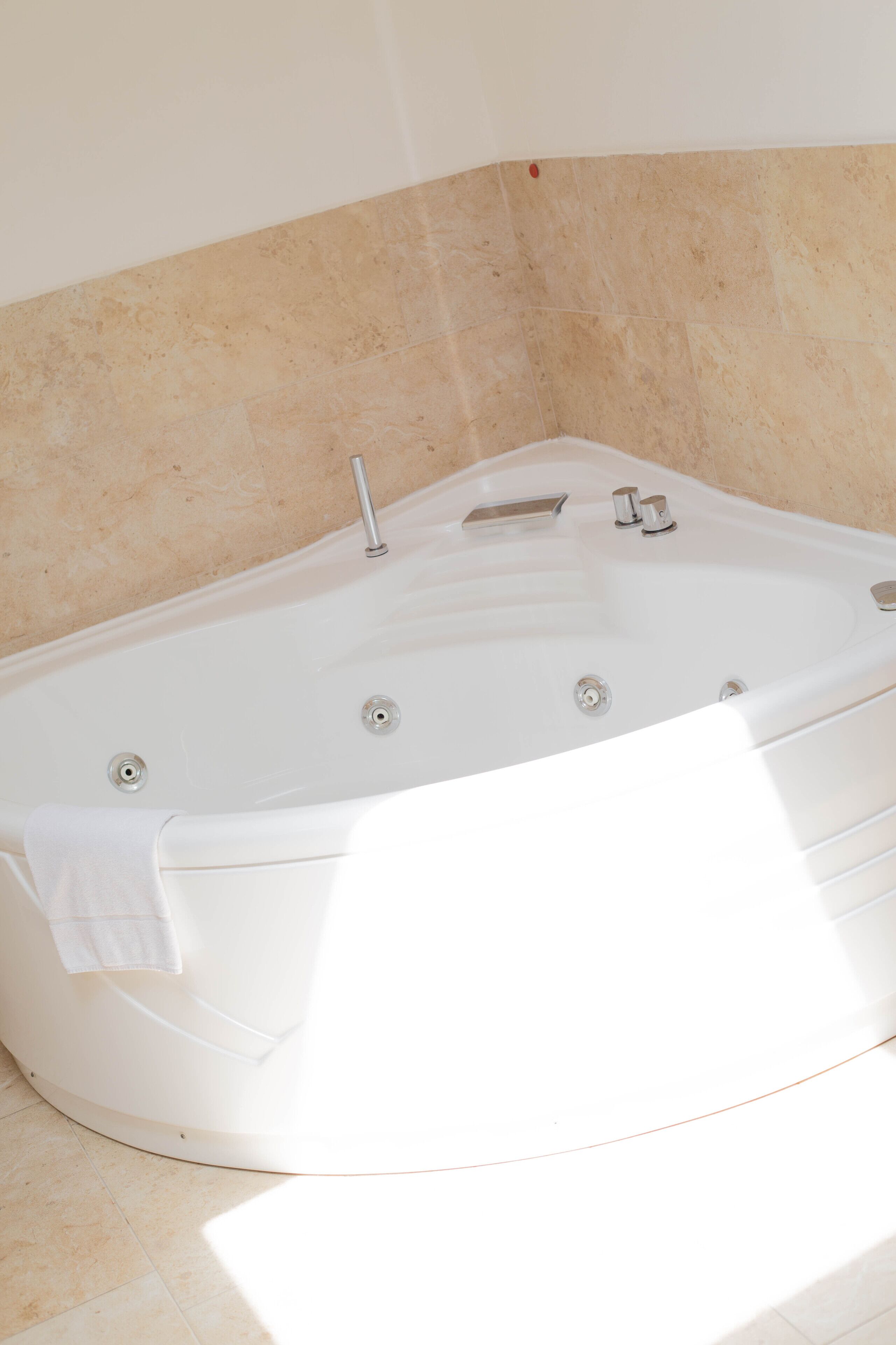 Una bañera blanca con un solo grifo y un cabezal de ducha manual, frente a una pared con azulejos color beige.
