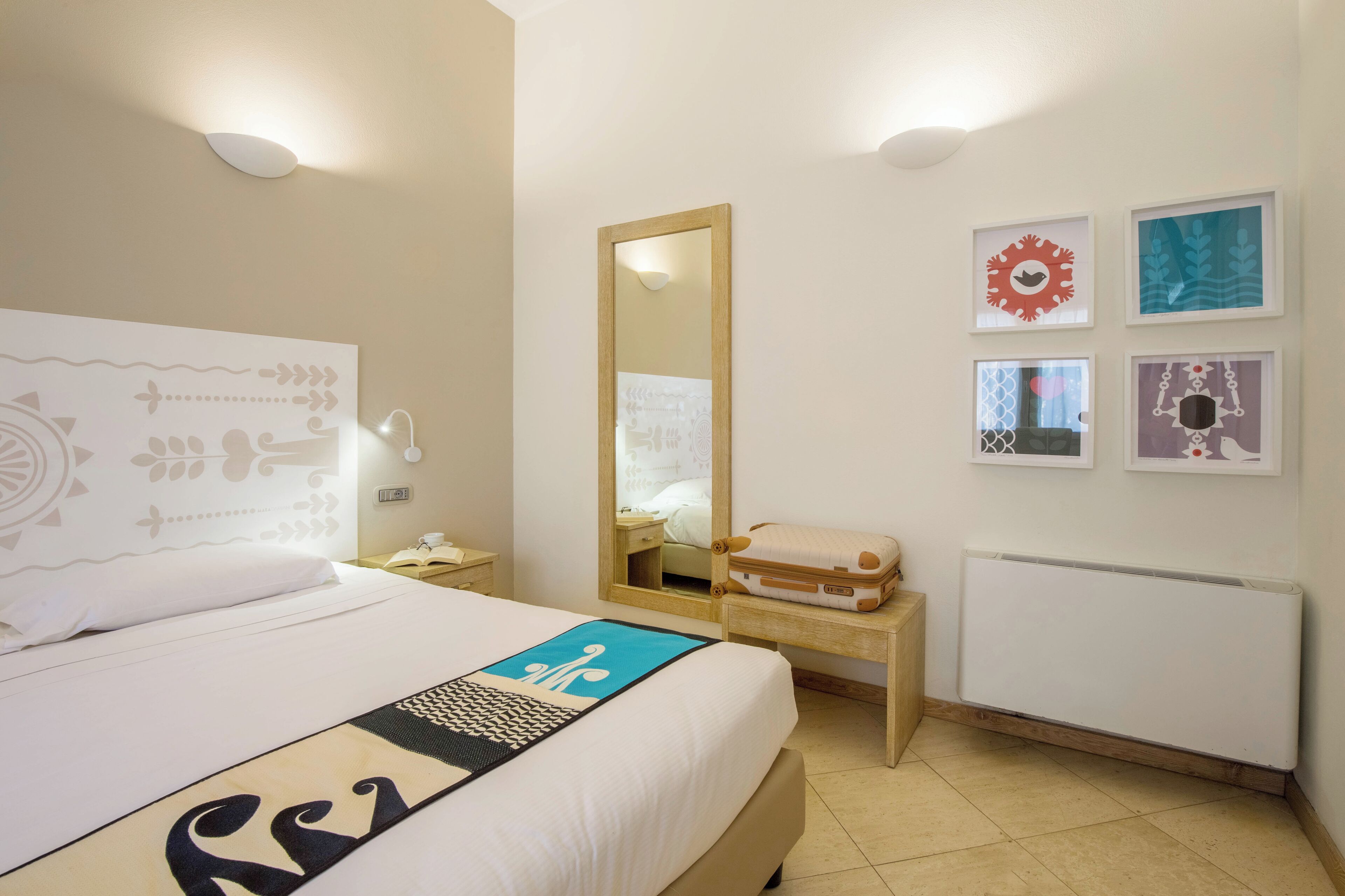 A hotel room with a bed, a bedside table, a mirror, a radiator, and wall art.