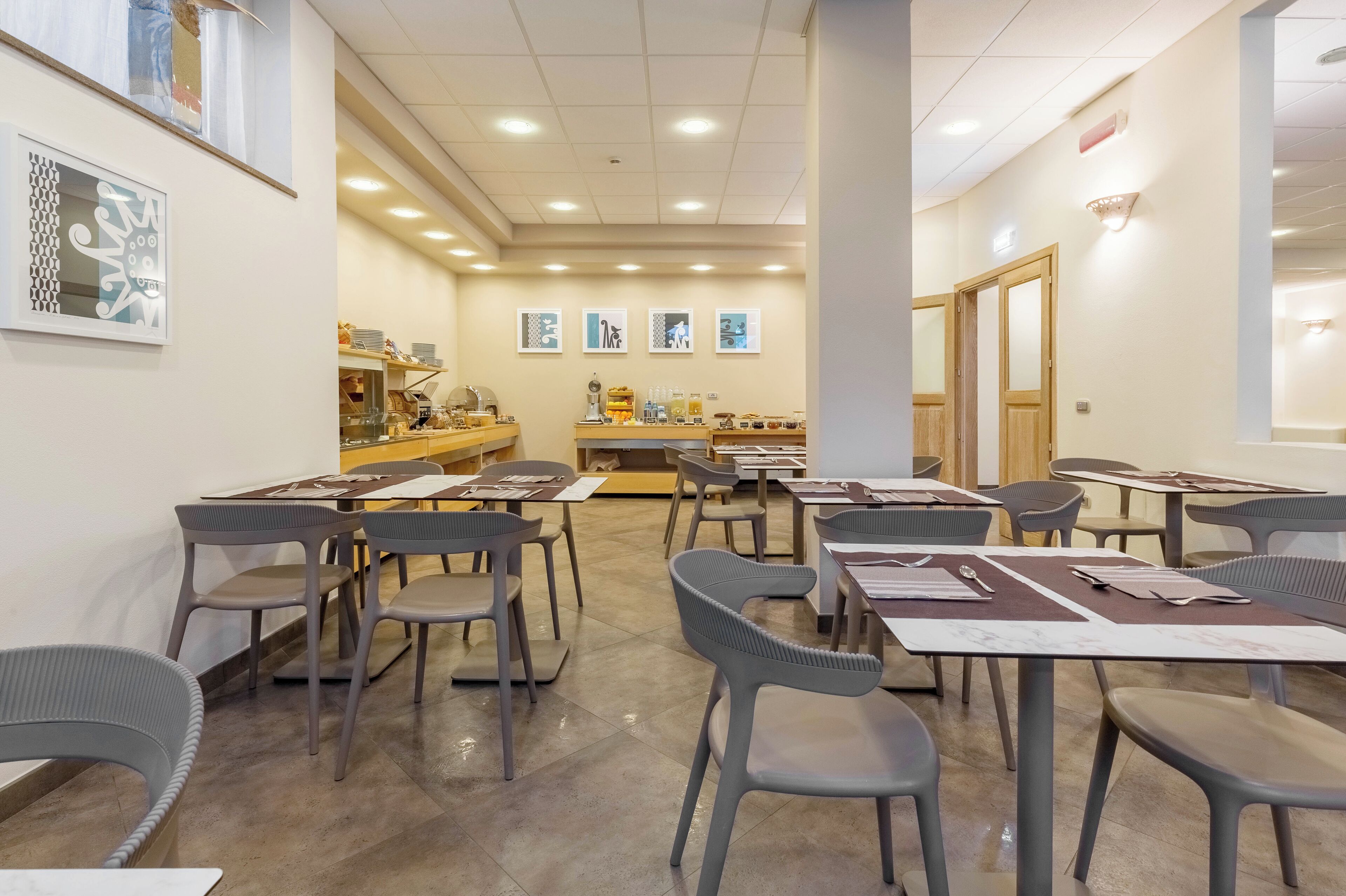 Zona pranzo con tavoli e sedie, cucina sullo sfondo e opere d'arte incorniciate alle pareti.