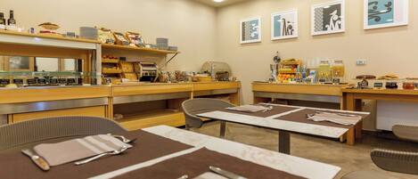 Un comedor con mesas dispuestas para comer, una estación de café y diversos alimentos exhibidos en estantes.