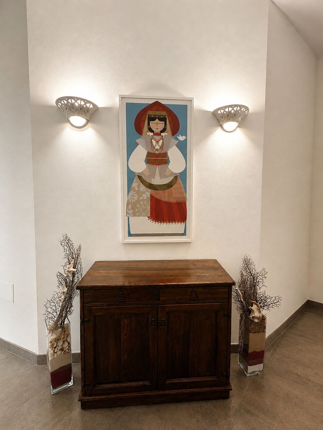 Paredes com uma obra de arte emoldurada, duas luzes fixadas e um armário de madeira com vasos decorativos.