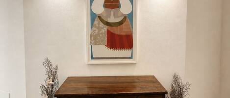 A wall with a framed artwork, two wall-mounted lights, and a wooden cabinet with decorative vases.